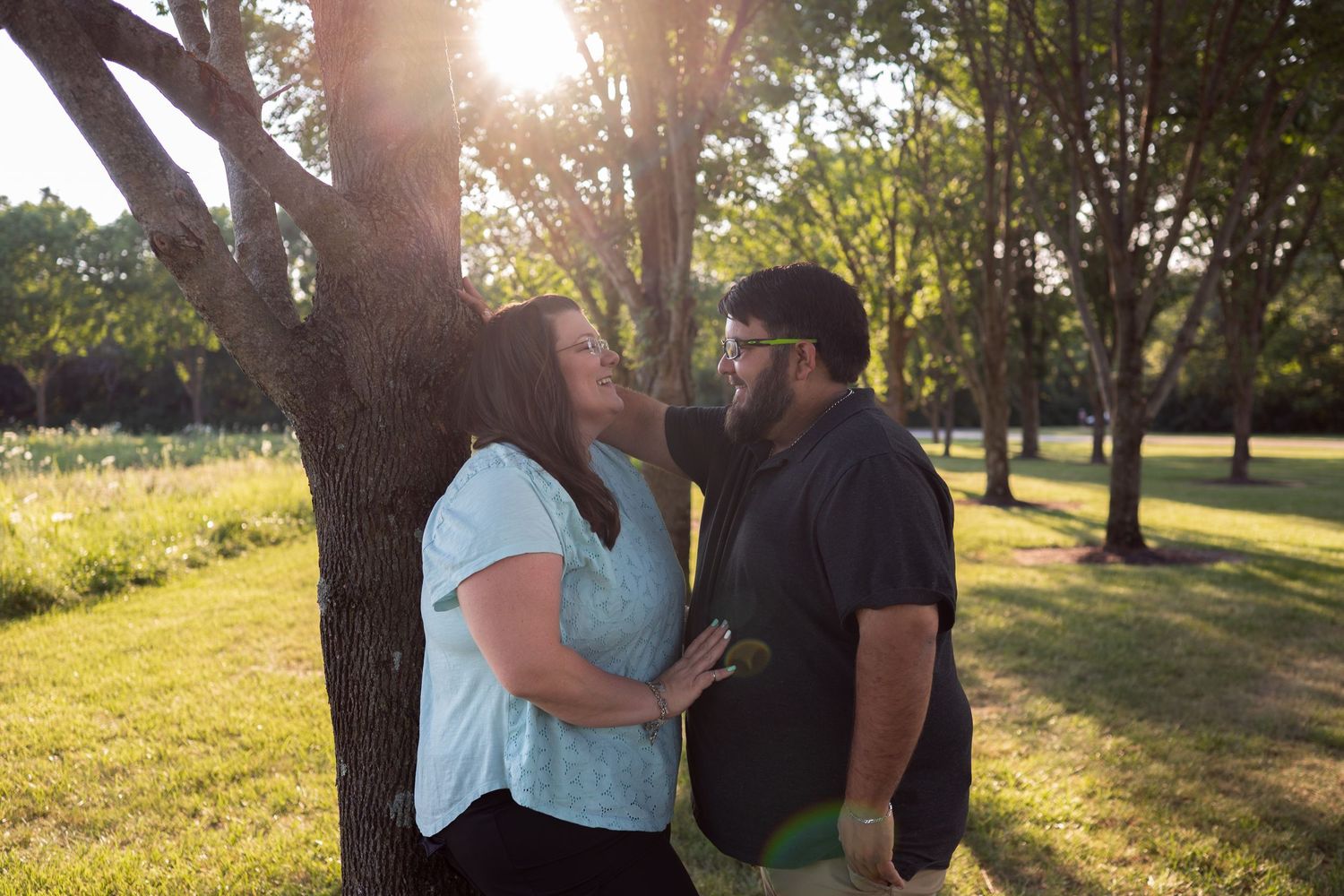 Couple sharing a romantic moment by a tree in a sunlit park during golden hour.
