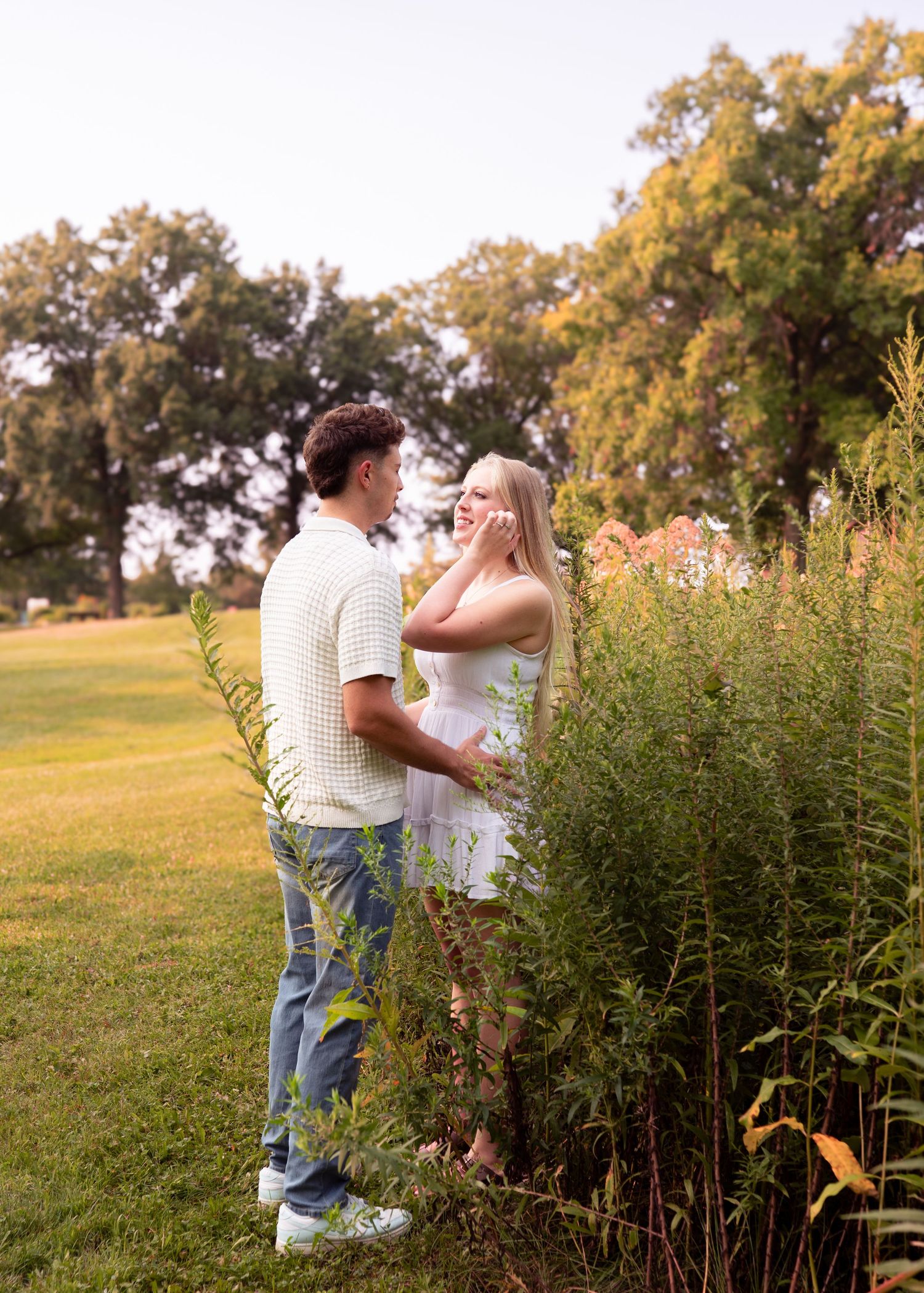 Couple laughing together near tall wildflowers in a lush green park during golden hour.