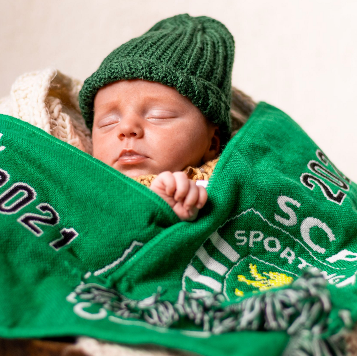 Baby resting with green sports-themed blanket and knit hat.
