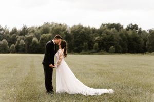 A romantic wedding couple shares an intimate moment in a serene meadow with trees in the background.
