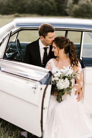 Newlyweds share a tender moment inside a vintage white car with beautiful florals.