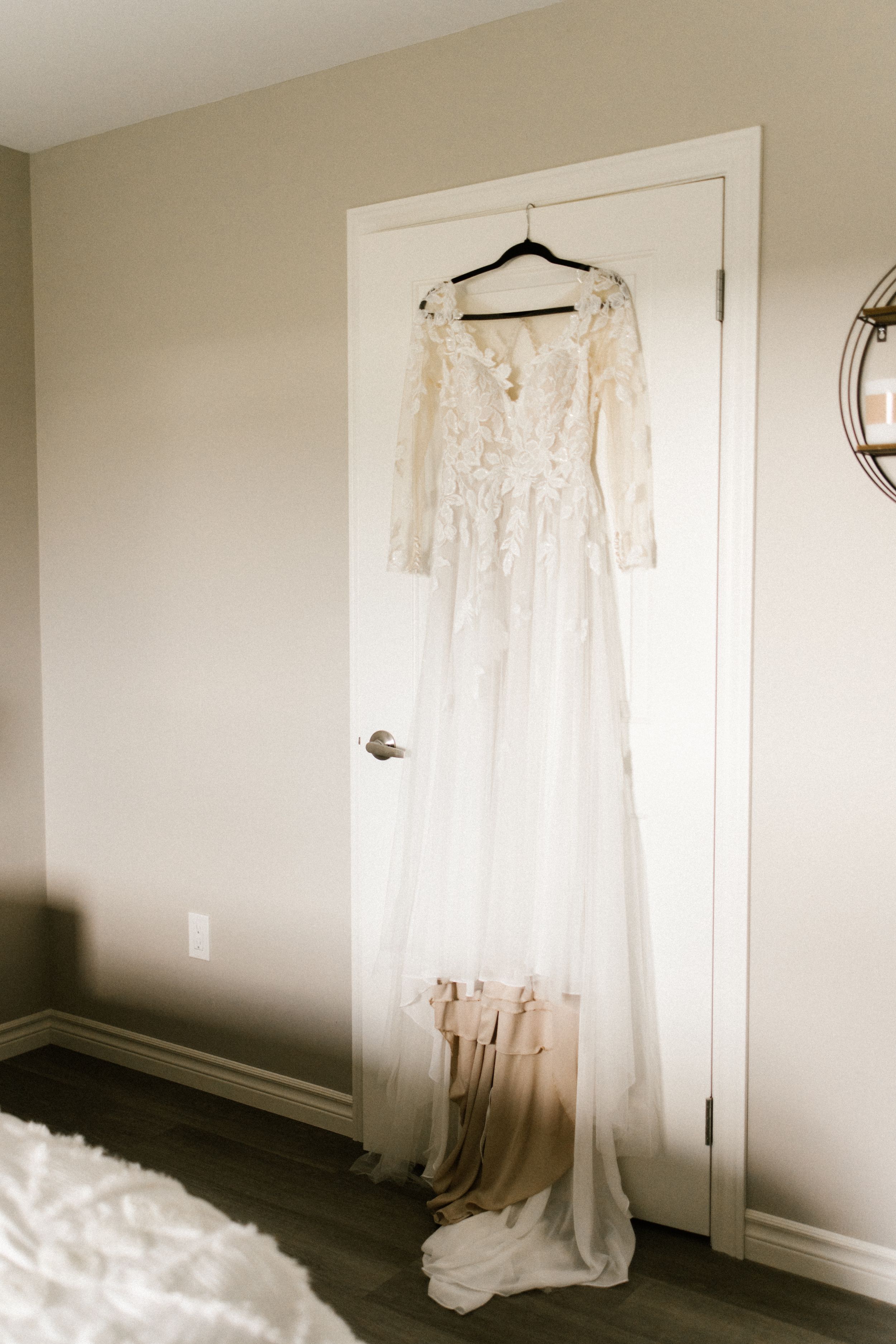 A delicate white lace wedding dress with long sleeves hanging on a door.