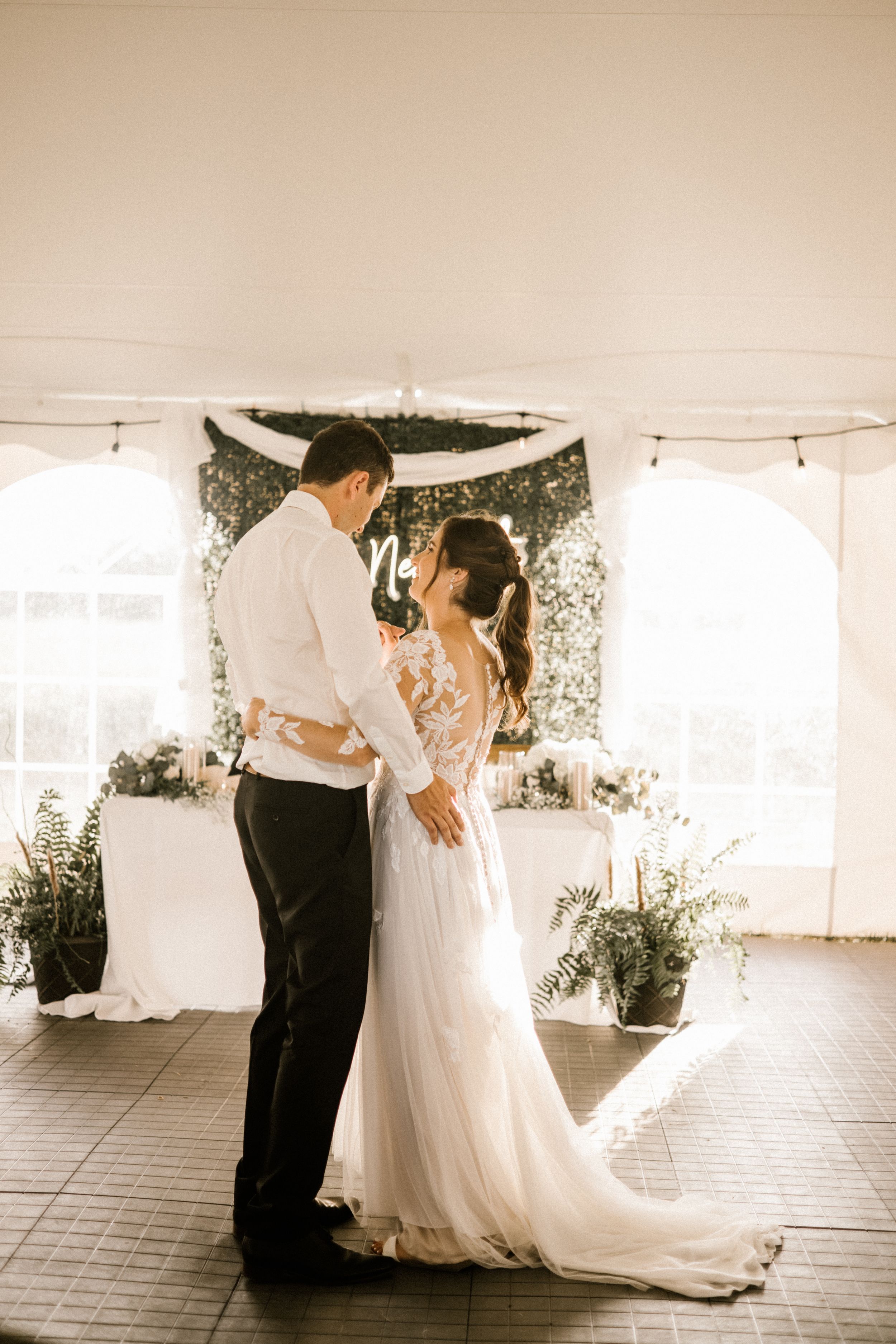 A couple dances beneath a decorated white tent during their wedding reception.