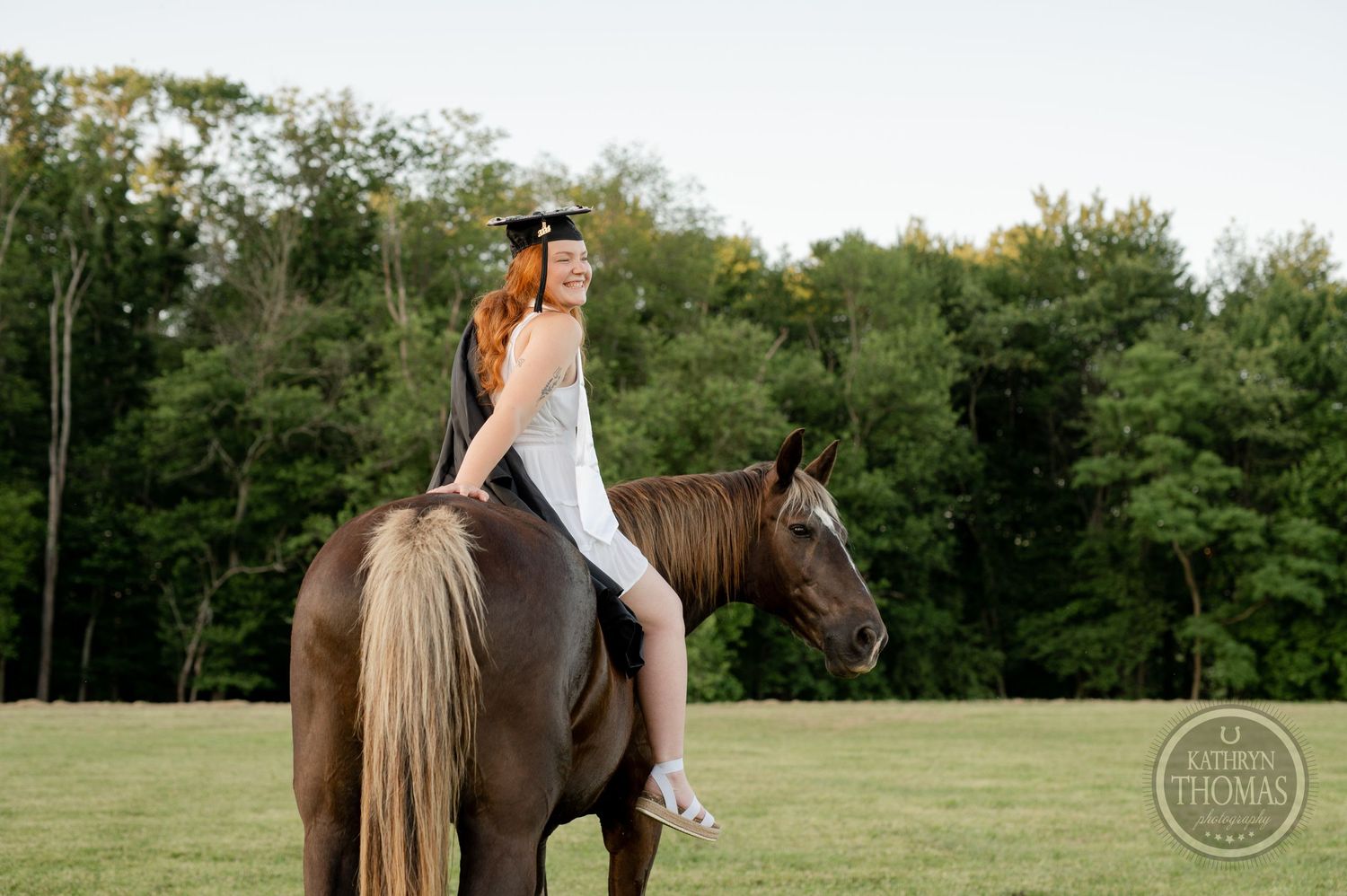 Person in riding attire sits atop a brown horse in front of a forest backdrop.