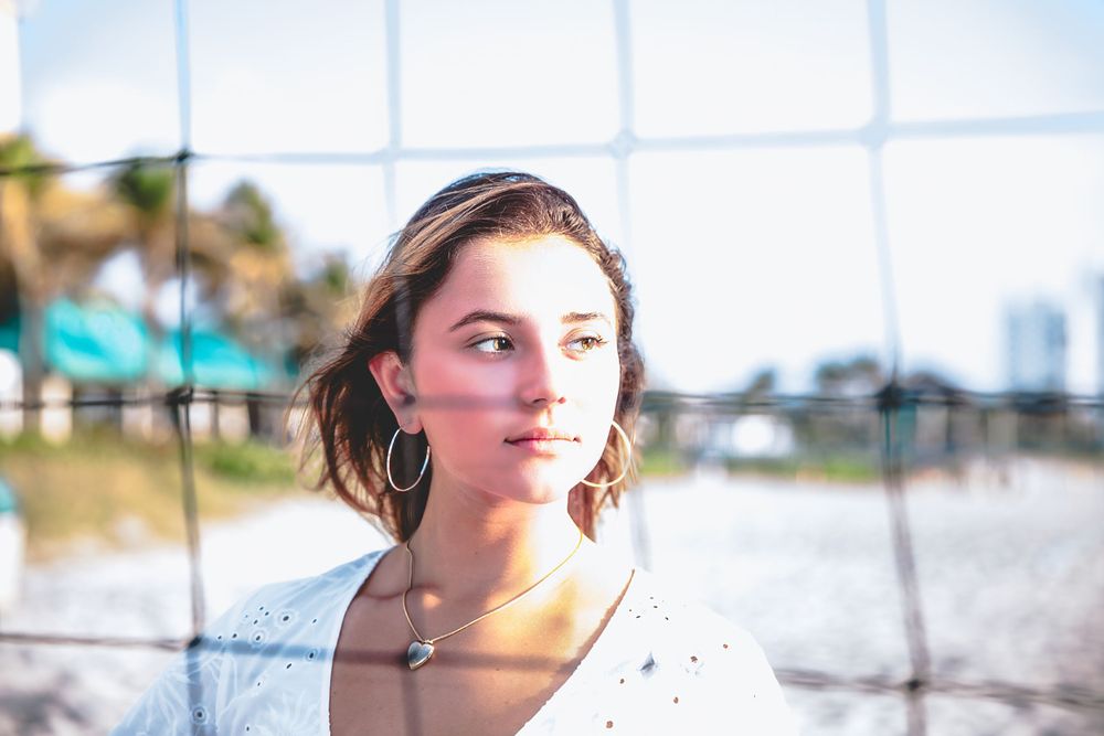 Artistic portrait through mesh fence with soft natural lighting capturing subject's profile.