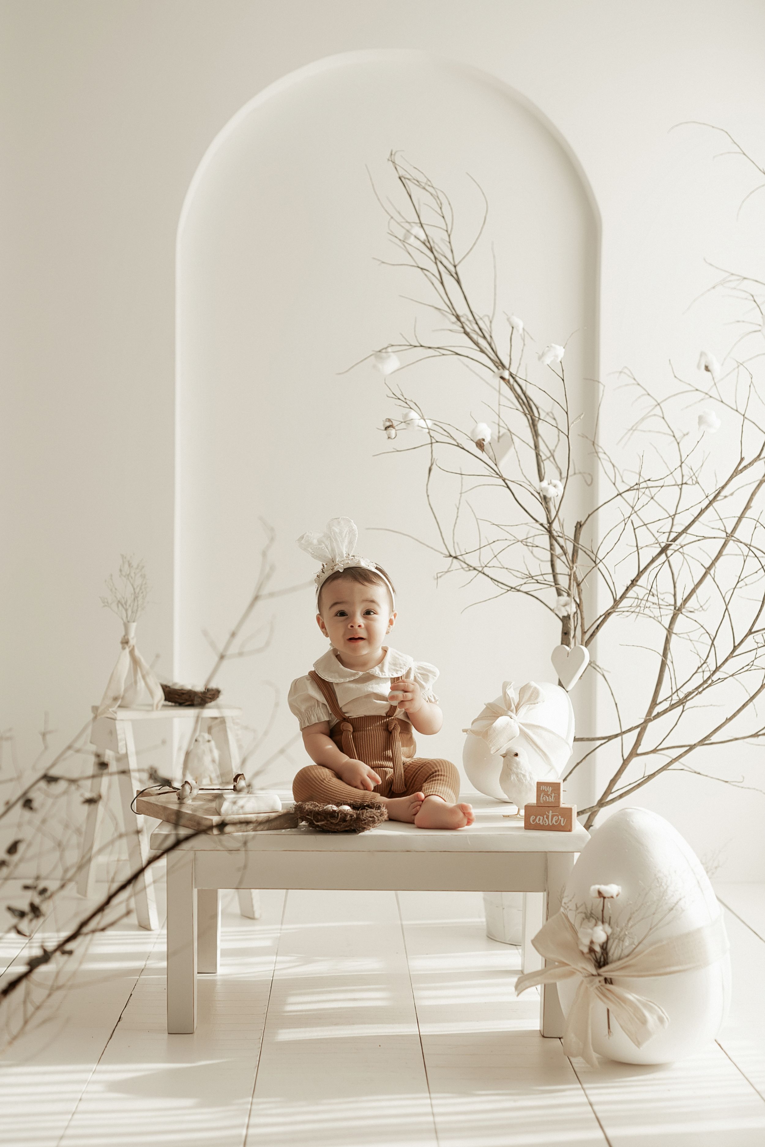 Minimalist white interior with decorative branches, ceramic vases and white bench in an arched alcove.