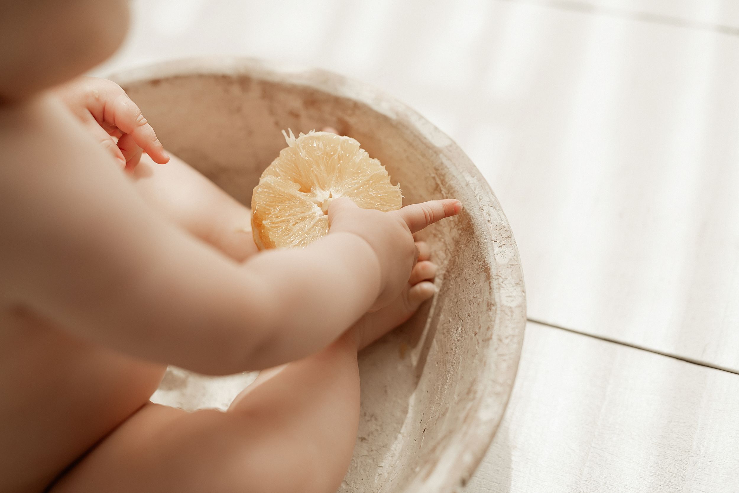 Small hands reach for a freshly peeled orange segment in a rustic bowl.