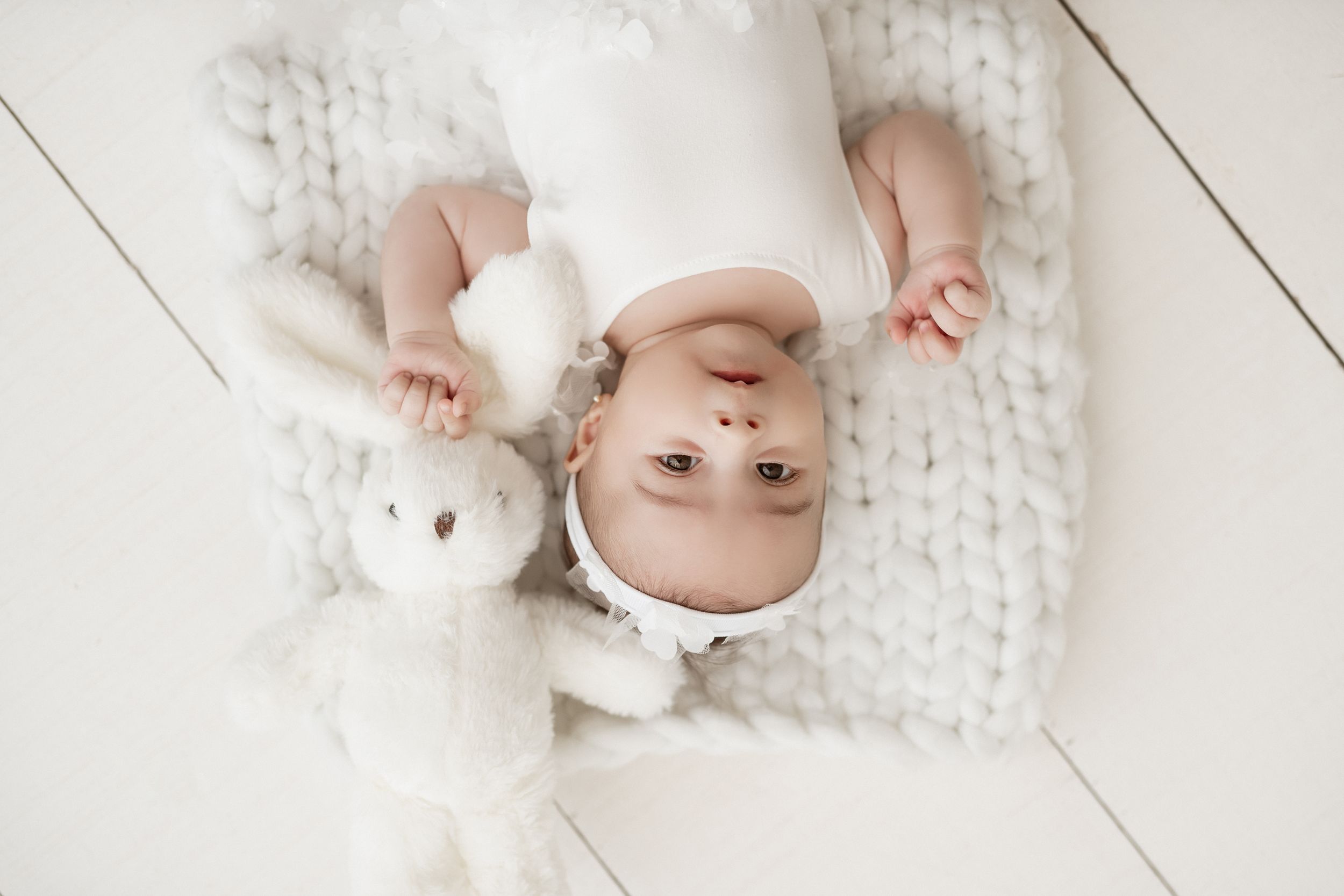 Baby lying on cozy knit blanket with white stuffed toy in soft natural lighting.