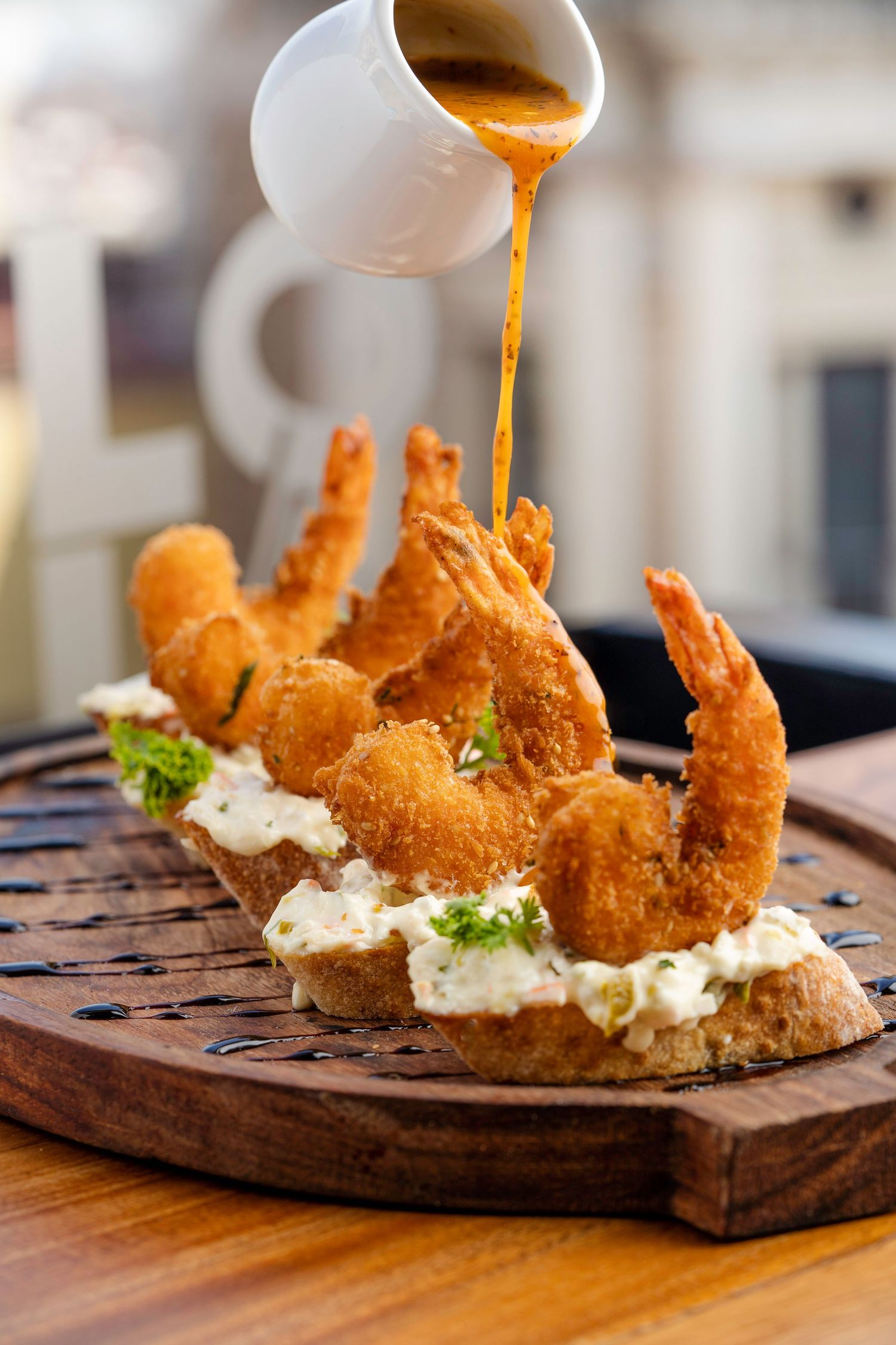 Crispy breaded shrimp served on a wooden board with sauce being drizzled on top.