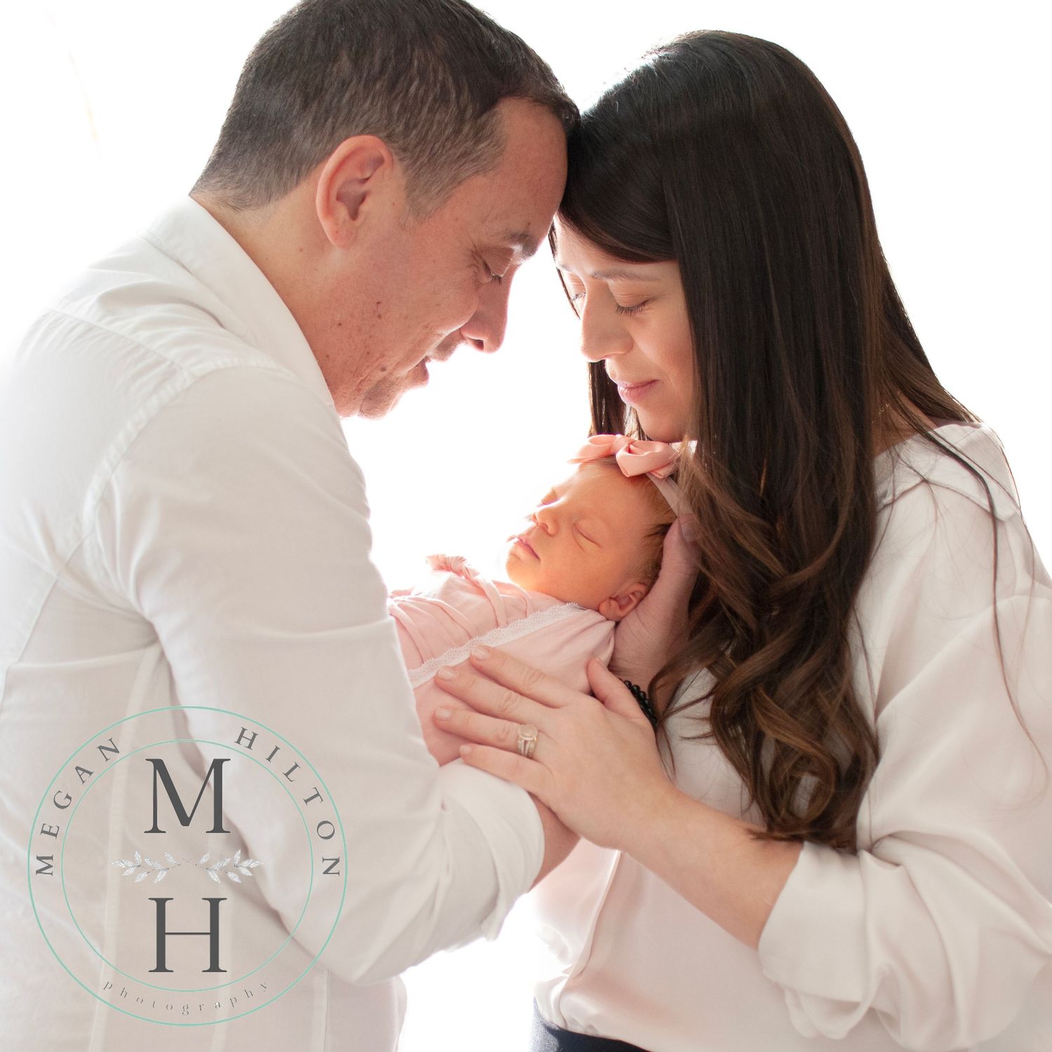 Mom and Dad holding newborn baby girl backlit