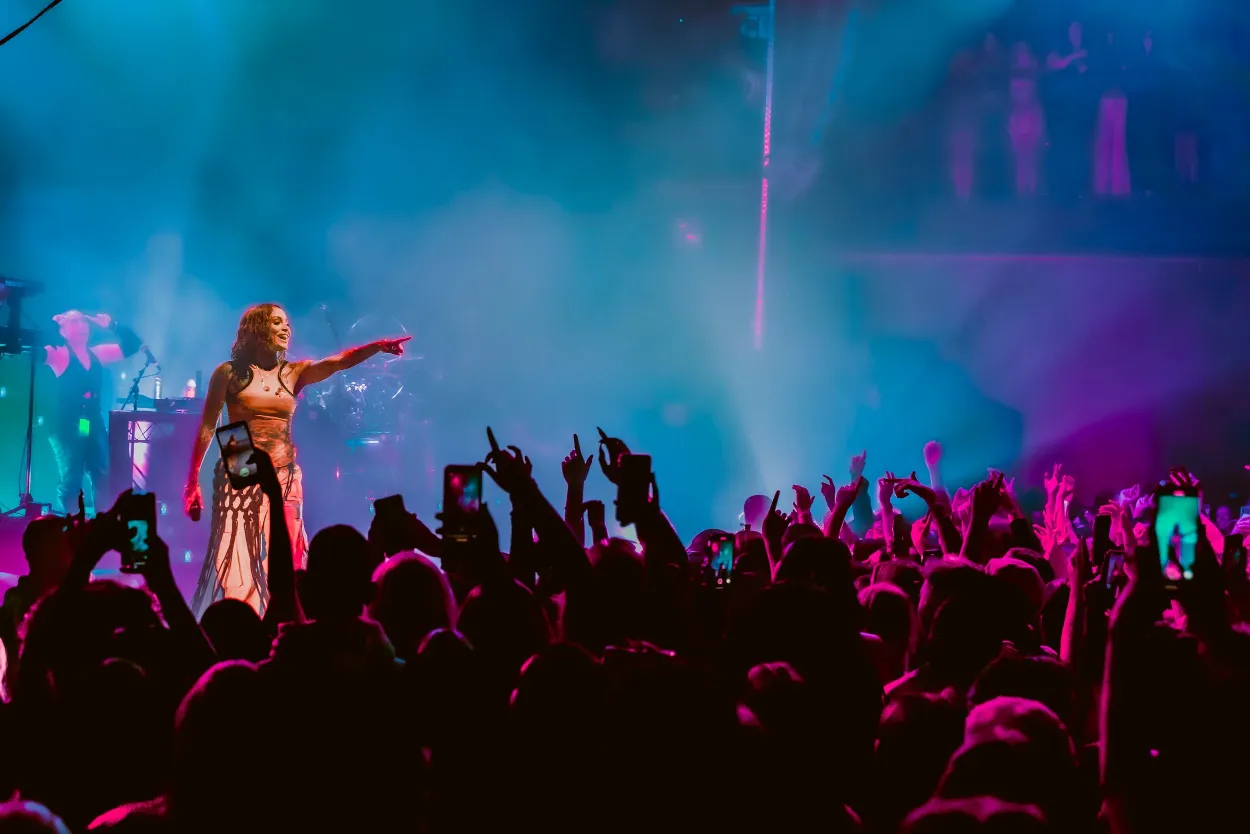 Silhouetted performer on stage with dramatic blue lighting and crowd raising hands.
