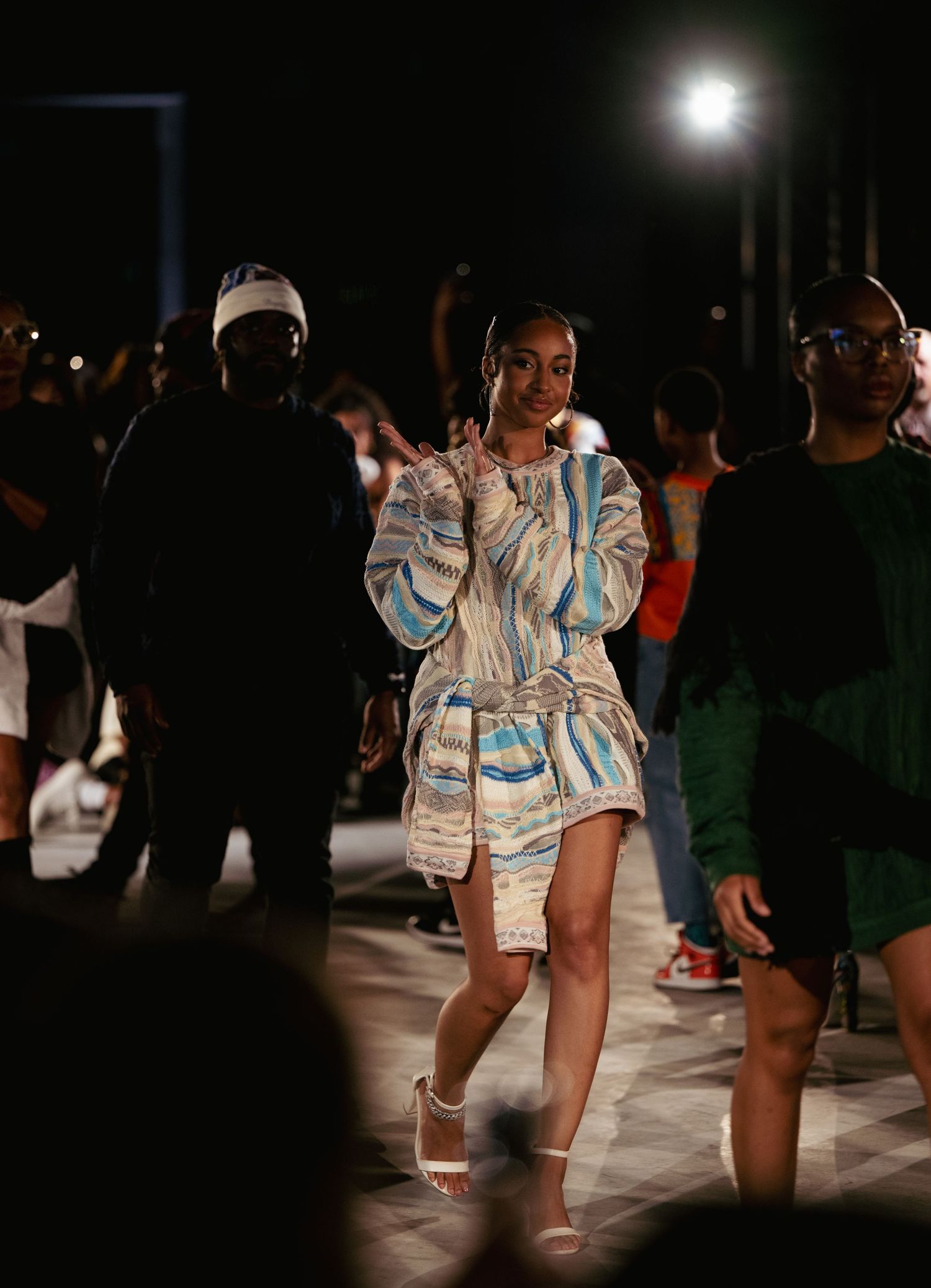 Fashion show model wearing a reflective silver-blue patterned ensemble on nighttime runway.