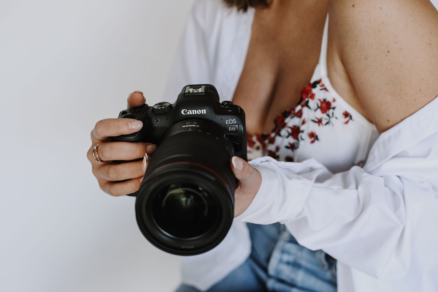 Person in white shirt holding professional camera against neutral background.