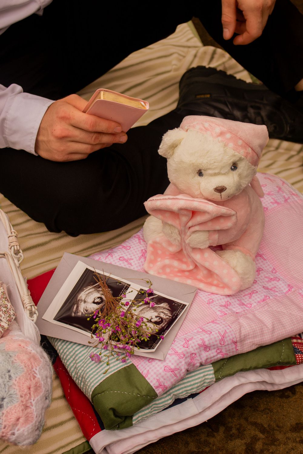 White teddy bear with pink blanket beside ultrasound photos and baby items on a bed.