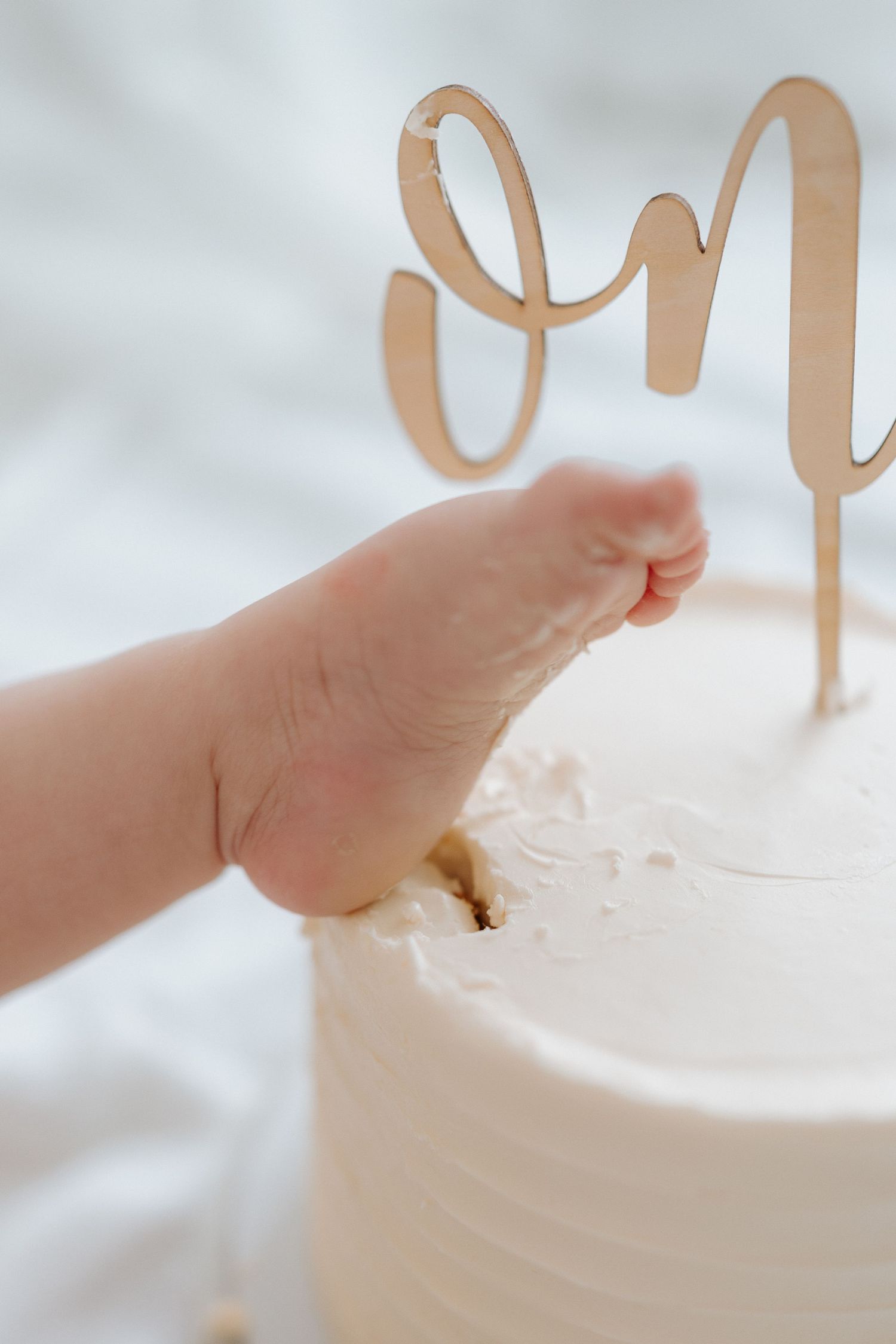 Small hand reaching for white frosted cake crumbs on wooden floor.