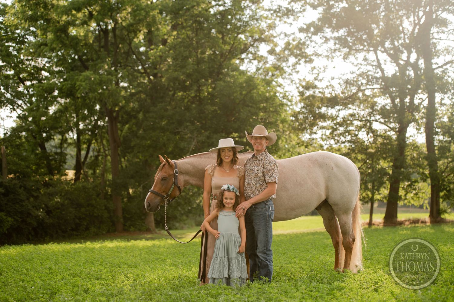 A family poses with their cream-colored horse in a serene meadow setting during sunset.