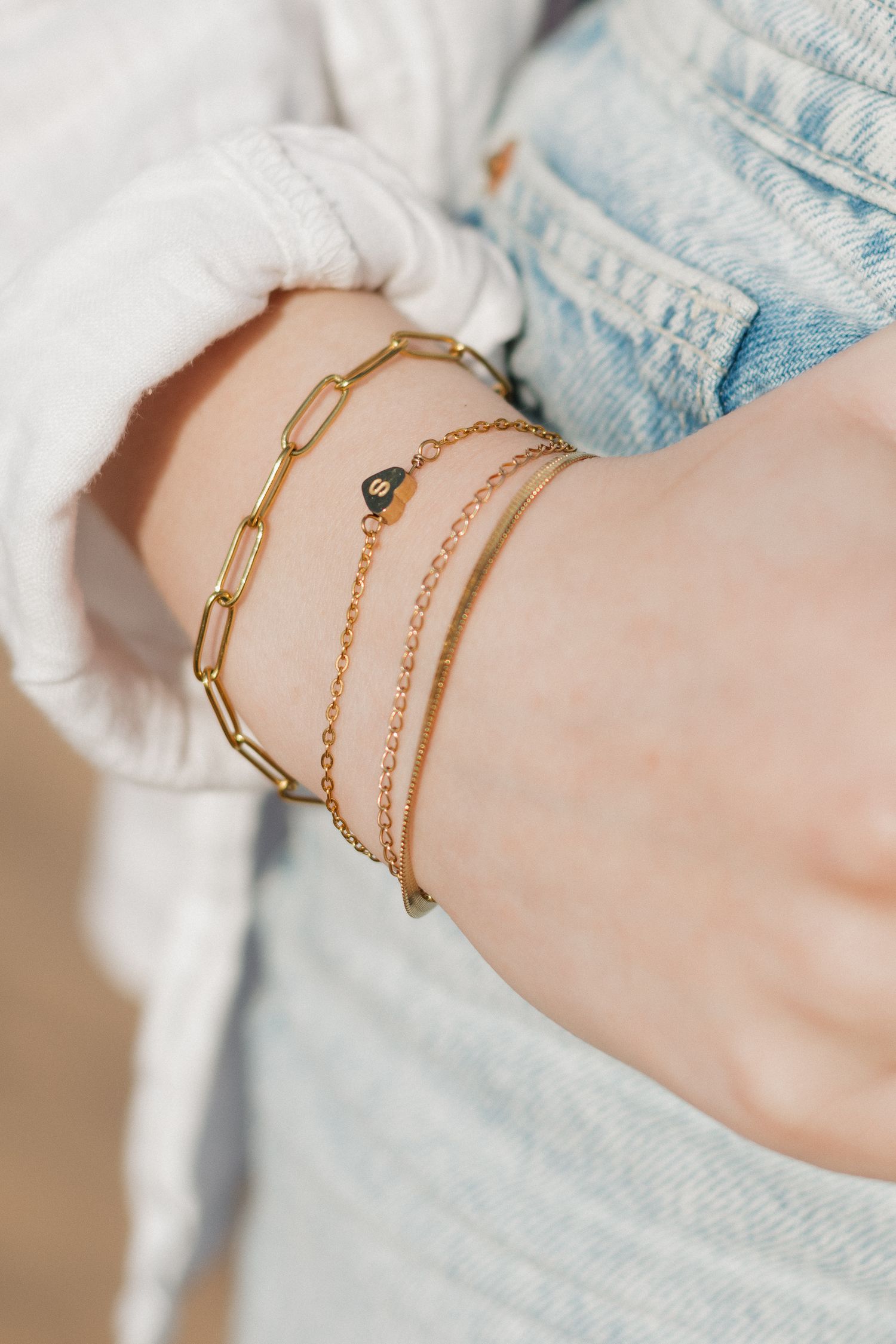 Delicate gold chain bracelets layered on a wrist against light denim and white fabric.