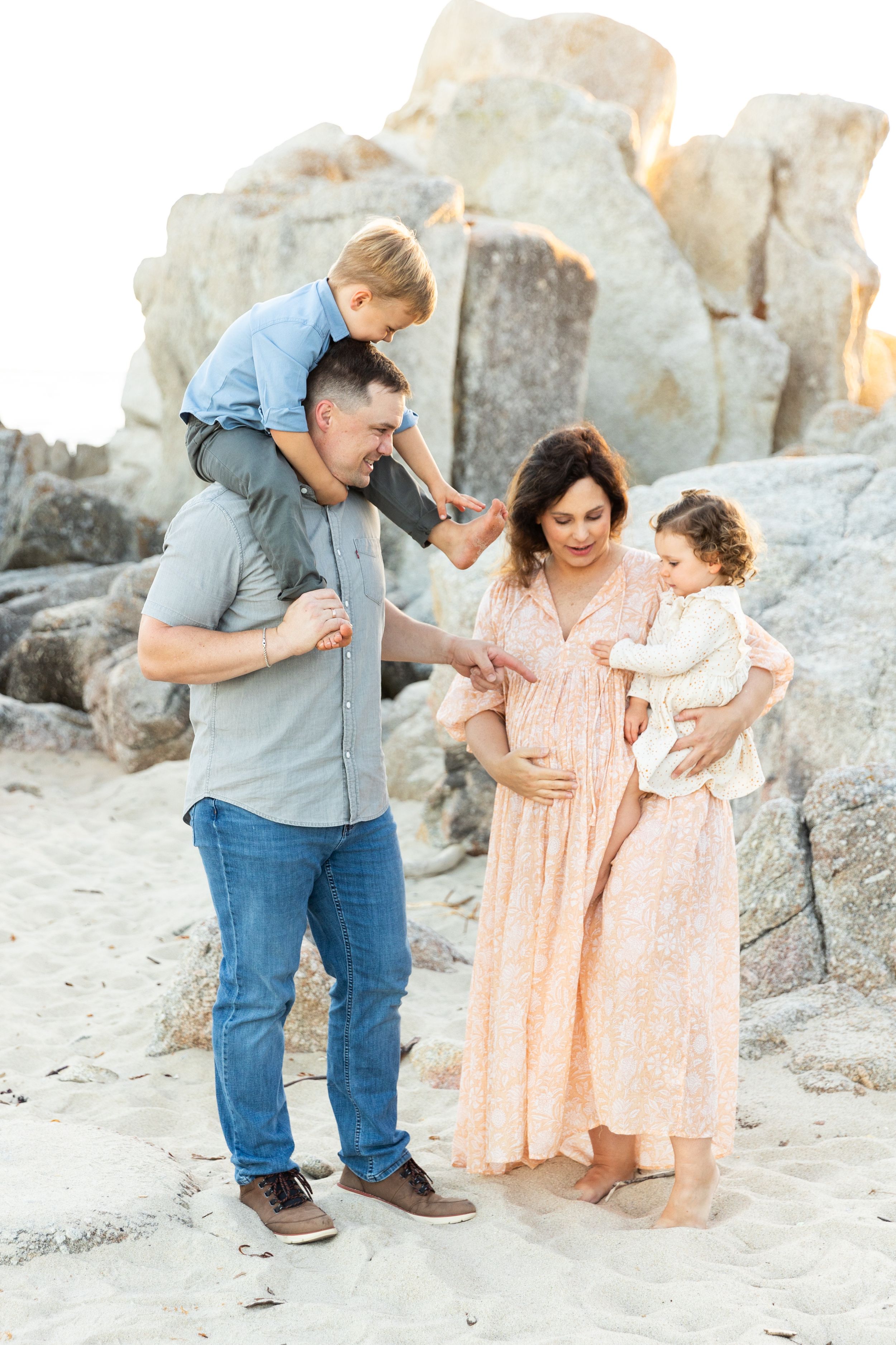 A family stands together on a rocky beach at sunset wearing coordinated pastel outfits in Carmel By the Sea, California.