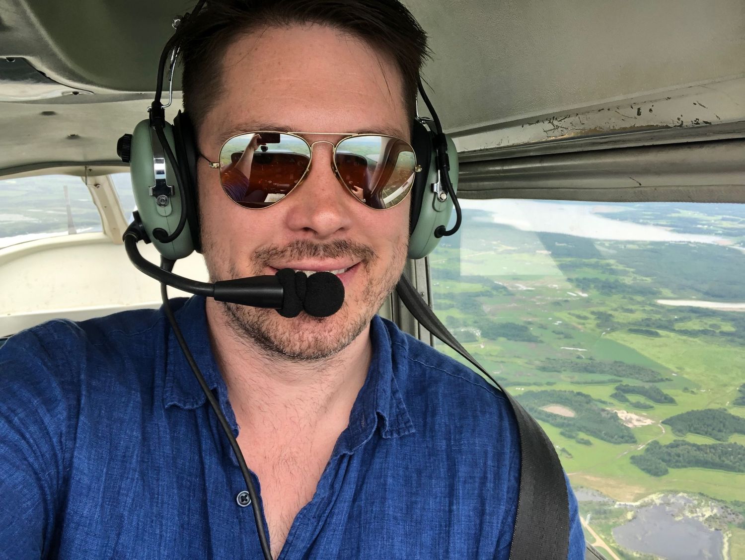 Photographer Evan Will pilot wearing aviation headset and sunglasses from cockpit with aerial landscape view below.