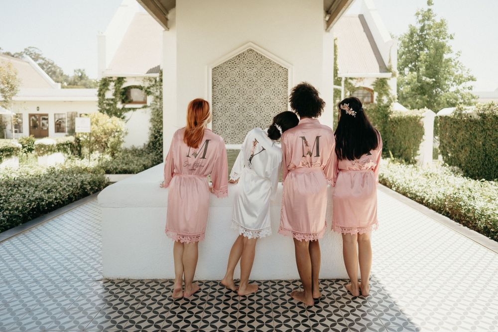 Wedding party members wearing matching pink robes standing together on tiled patio.