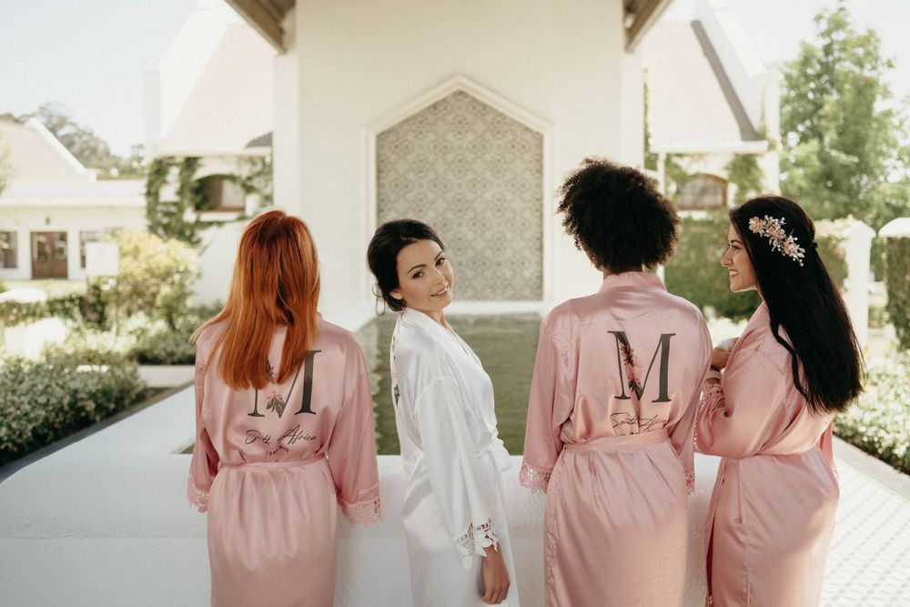 Bridesmaids in pink robes with monogrammed details getting ready before the wedding.