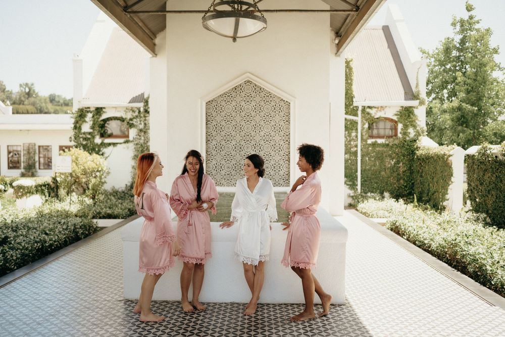 A group in pink dresses poses together under a covered outdoor walkway at a wedding venue.