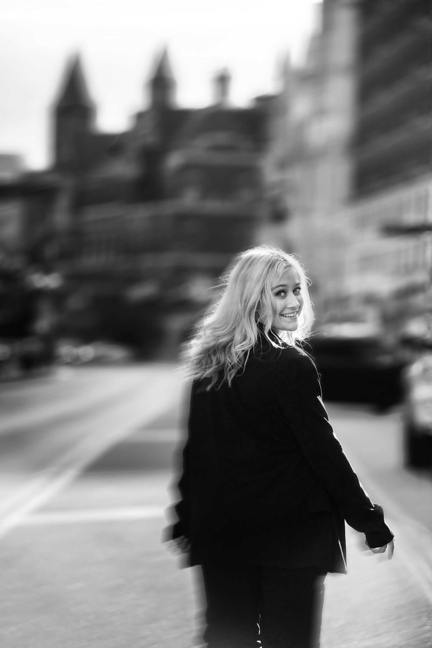 Black and white street photography with person in dark coat against city architecture.