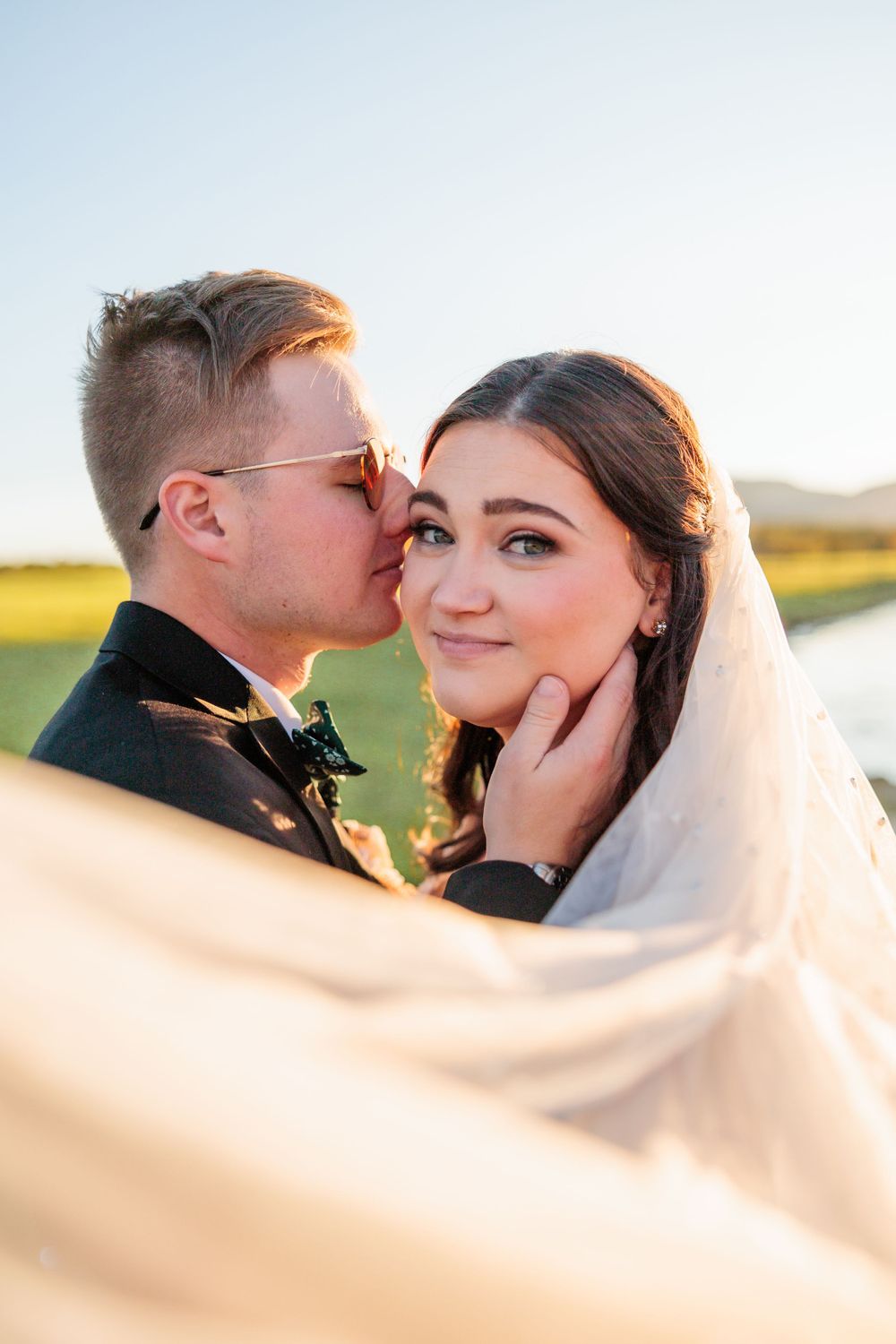 Romantic moment captured between newlyweds during golden hour by the water.