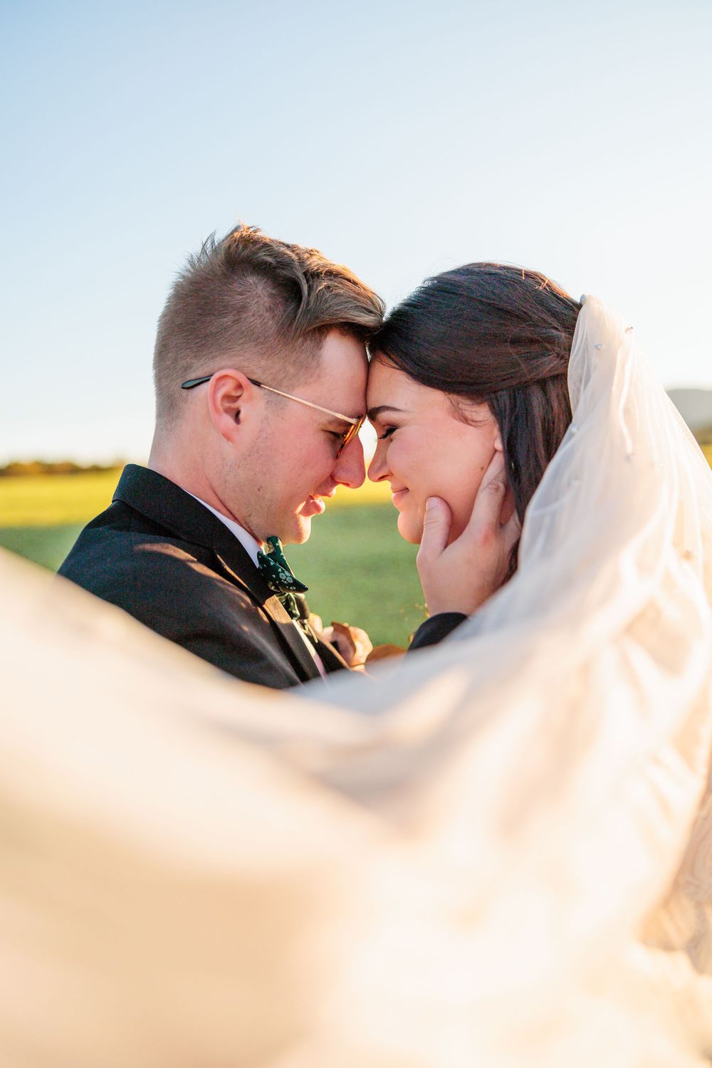 Intimate wedding moment captured through flowing veil during golden hour.