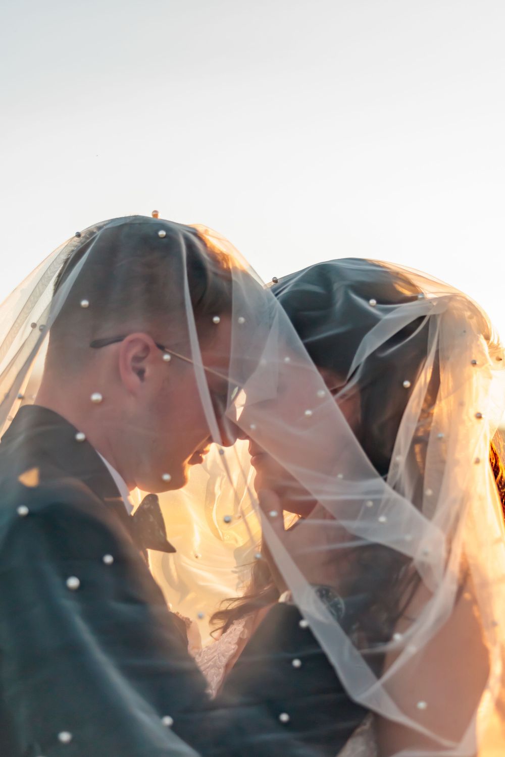 Romantic sunset portrait through delicate bridal veil creating dreamy effect.