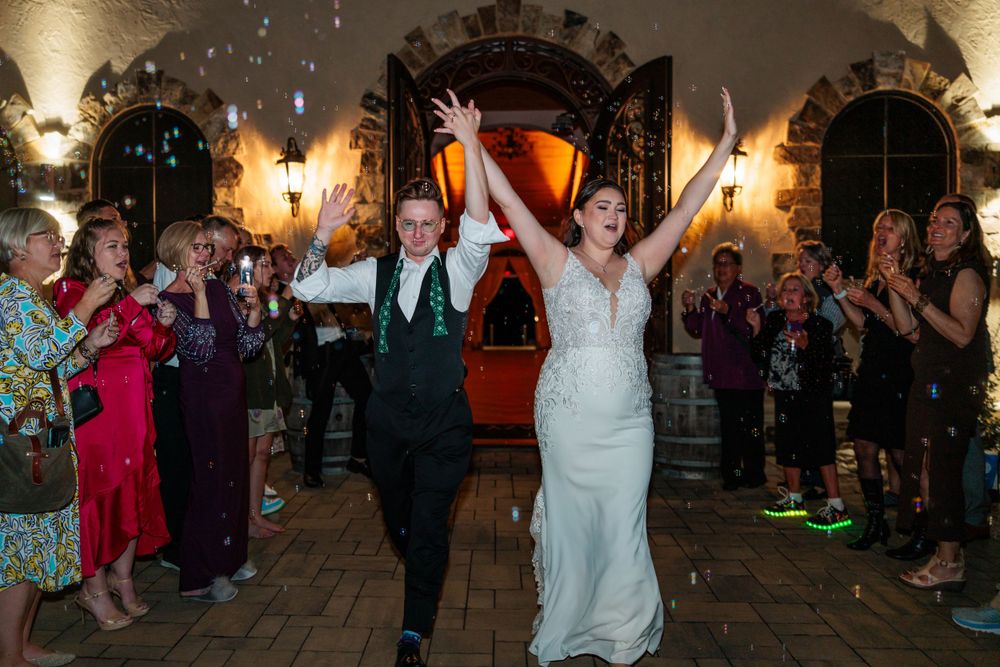 Wedding couple triumphantly exits their reception while guests line the pathway applauding their departure.