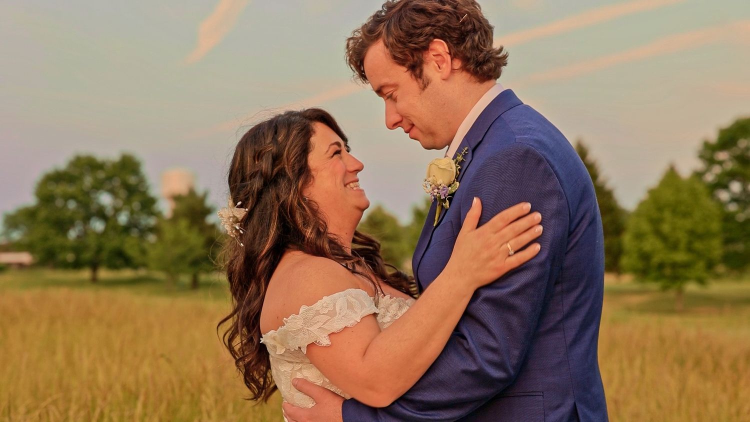A couple shares a joyful moment together while standing in a golden wheat field at sunset.