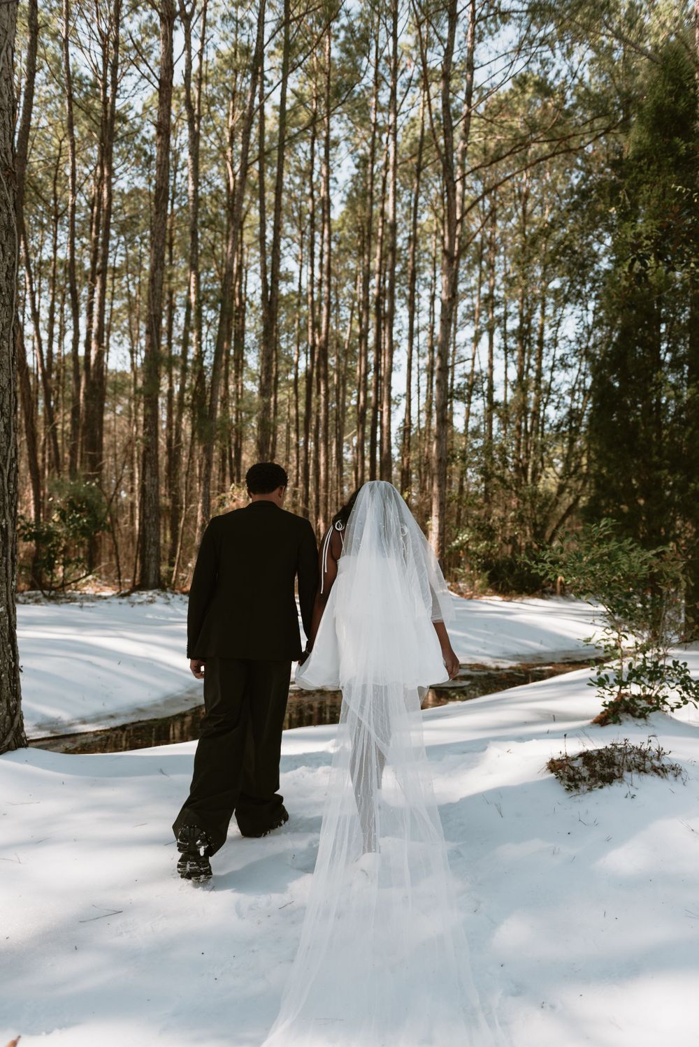 A bride and groom walking in the snow together with hand in hand.