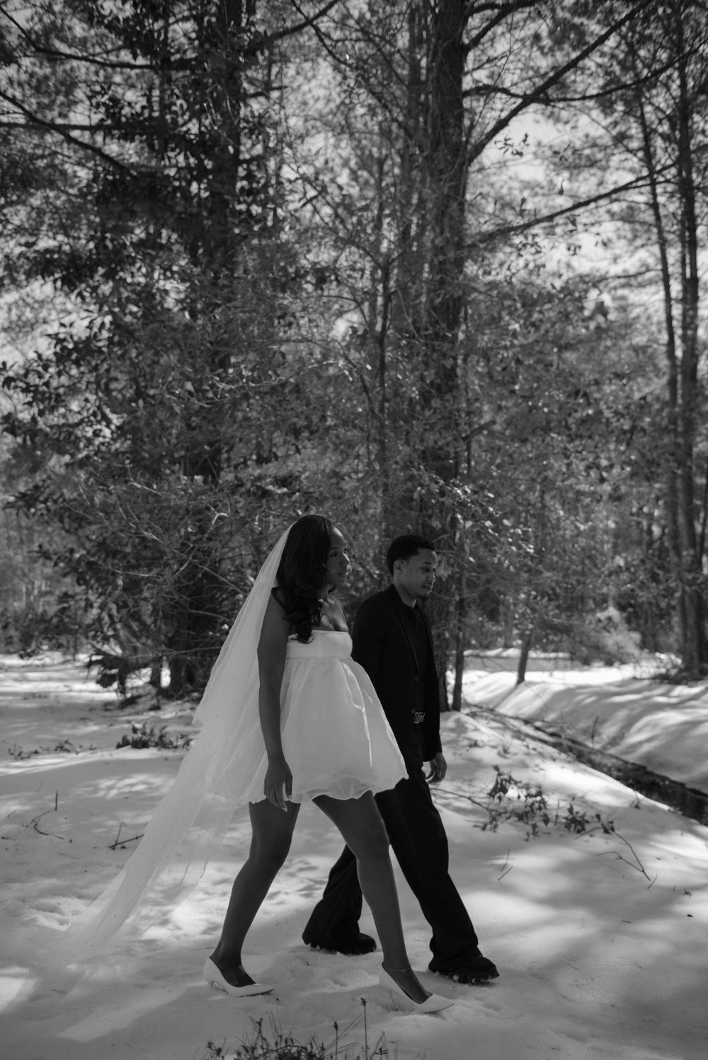 A black and white photo of a bride and groom walking together in the snow.