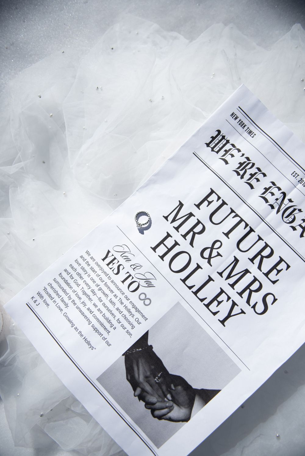 A newspaper announcement of an engagement with a diamond ring on top of the paper sitting on snow.