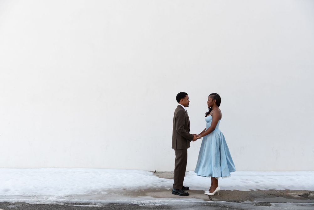 A portrait of a couple posing, staring face to face with snow surrounding them on the ground.