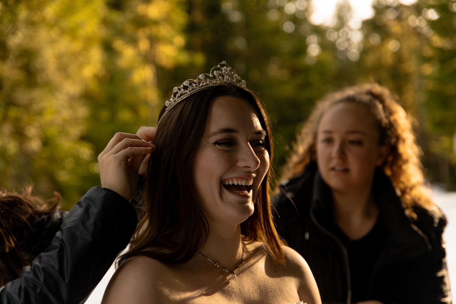 A joyful winter wedding moment with laughing women in sunlit forest.