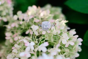 A sparkling diamond engagement ring nestled among delicate pink and white hydrangea blooms in a garden setting.
