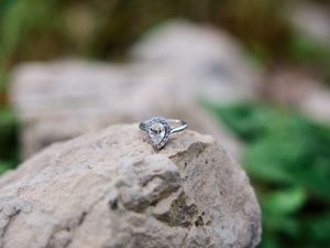 A sparkling diamond engagement ring displayed on natural stone with greenery in the background.
