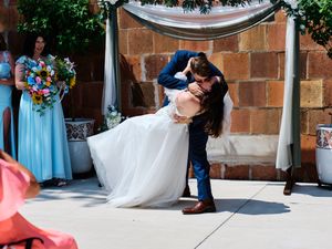Wedding couple shares a romantic dip and kiss during their first dance at an outdoor reception venue.