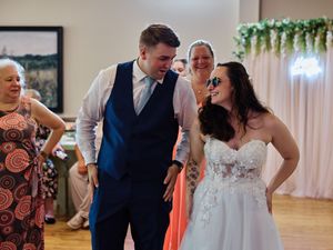 Wedding guests dance and celebrate together on a wooden dance floor at an indoor reception venue.