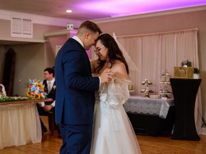 A couple shares an intimate dance moment at their wedding reception under purple lighting.