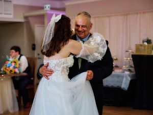 Wedding guests dancing together in a reception hall with white drapes and ambient lighting.