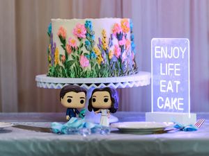 A decorative cake display setup with neon signs, Funko Pop figures, and pastel colors in a party setting.