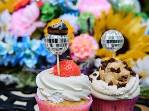 Colorful cupcakes decorated with whipped cream, disco balls, and chocolate chip toppings on a festive dessert table.