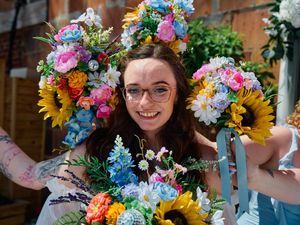 A vibrant floral crown featuring sunflowers, pink roses and blue delphinium creates a cheerful summer garden display.