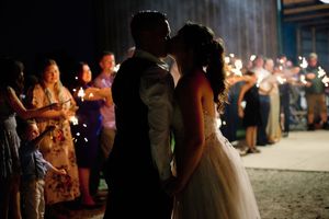 Wedding guests dance and celebrate at a nighttime beach reception with sparklers illuminating the festive atmosphere.