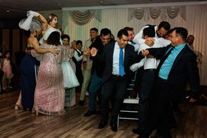 Wedding guests dance and celebrate together on a wooden dance floor at an indoor reception venue.