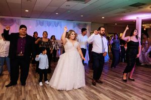 Wedding guests dance together on a wooden floor illuminated by colorful purple and blue lighting at a reception.