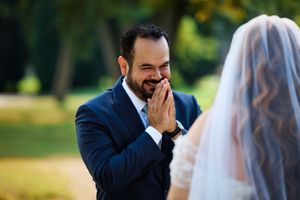 A groom in a navy suit shows an emotional first reaction during a wedding ceremony outdoors.